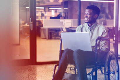 Man in a wheelchair smiling and holding a laptop