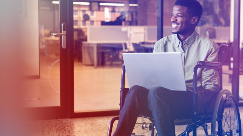 Man in a wheelchair smiling and holding a laptop