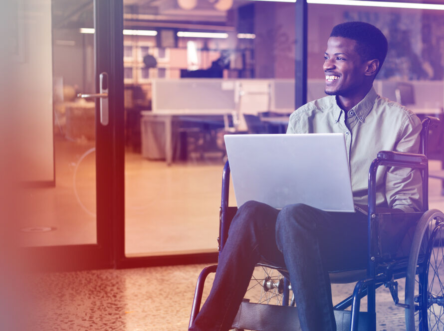 Man in a wheelchair smiling and holding a laptop