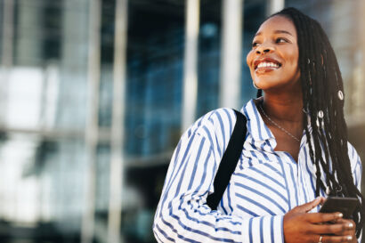 Woman smiling on the street holding a mobile phone.