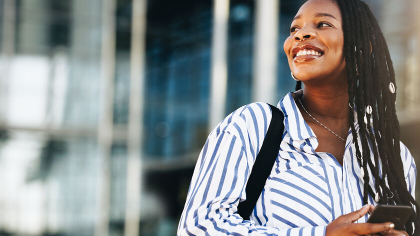 Woman smiling on the street holding a mobile phone.