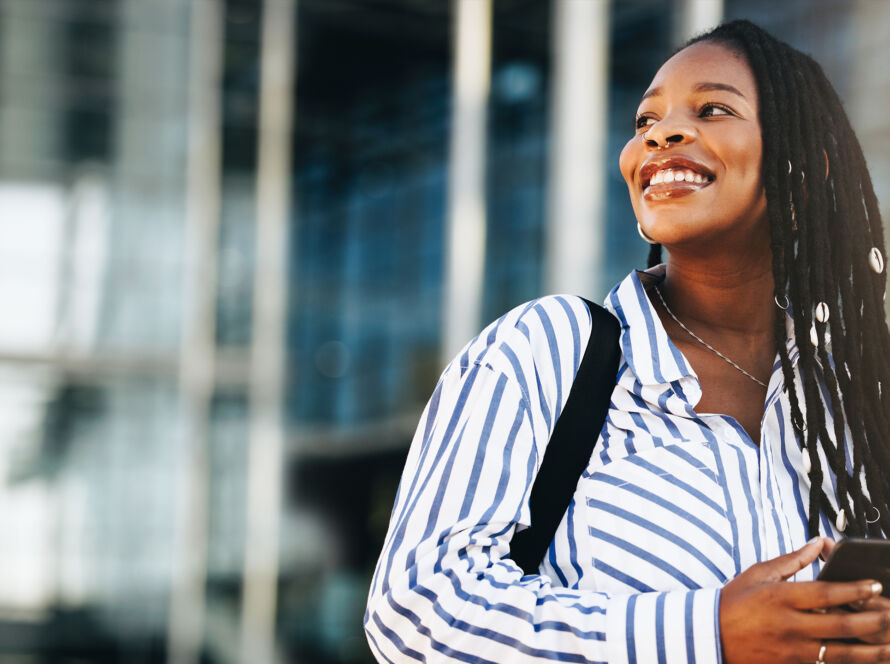 Woman smiling on the street holding a mobile phone.